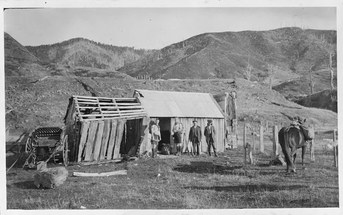 Trampers George Moir and Cyril Woods with two deer stalkers outside Bassett's Hut, Waiohine Valley, Tararua Ranges