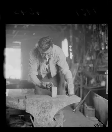 Image: Unidentified blacksmith working at an anvil, in a workshop, Johnsonville, Wellington