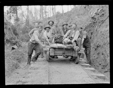Image: Group portrait of unidentified forestry workers pushing a log rail carriage within an unknown forest, Kakahi District, Manawatu-Whanganui Region