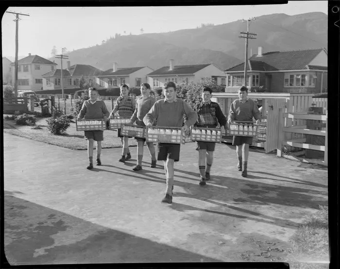 Schoolboys carrying crates of milk across school ground