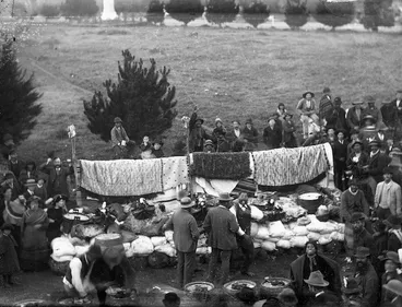 Image: Crowd surrounding a rack of Maori cloaks and a pile of produce