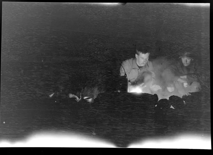 Edgar Williams and Jack Lye sitting around a campfire at night, during mountaineering trip, [Waimakariri Valley, Canterbury Region?]