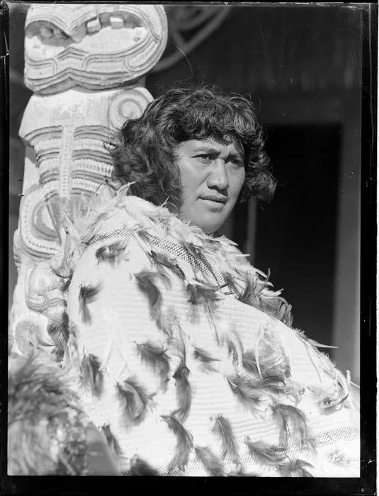 Portrait of Pura Hohepa Konui sitting next to a carved pou at Otūkou marae, Lake Rotoaira