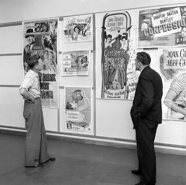 Image: Two men looking at a group of posters on a wall advertising movies