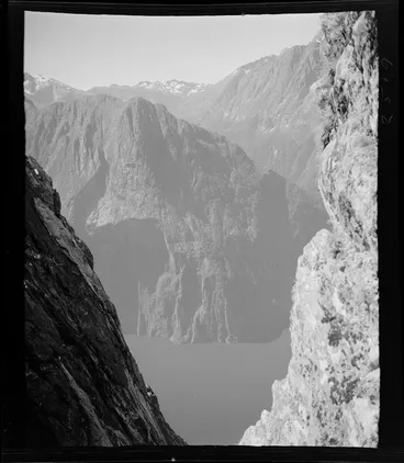 Image: Part one of a stereograph showing a view into fiord between steep rock faces, including mountains behind, Milford Sound