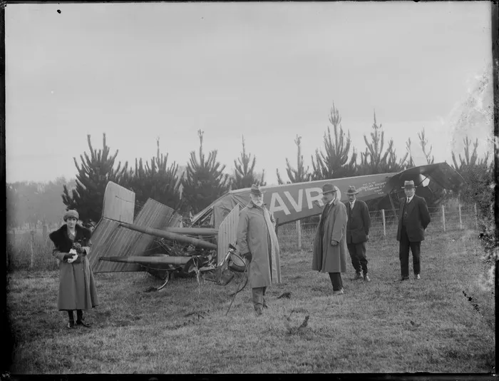 An AVRO aircraft, made by the Australian Aircraft & Engineering Company Ltd, in a field after an accident, with an unidentified woman and four unidentified men standing alongside it, possibly Hawkes Bay region