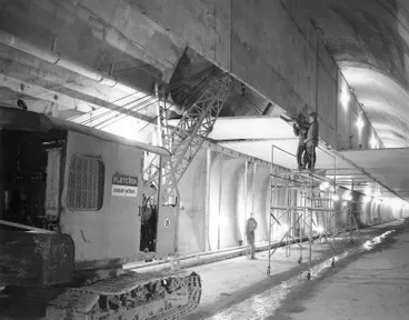 Image: Fletcher Holdings Ltd - Thorn Products Ltd: 1963 Christchurch-Lyttelton Road Tunnel - Erection of 3-ton slab (700 lbs of tiles) the prestressed slab is 12' x 13'3 x 3"; On left is fresh air duct; On right exhaust duct