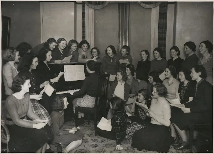 Women gather around piano at YWCA Hostel, Boulcott Street, Wellington - Photograph taken by William Hall Raine