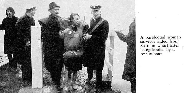 A barefooted woman survivor aided from Seatoun wharf after being landed by a rescue boat