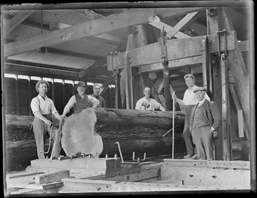 Image: View of unidentified workers within the Kakahi Sawmill in the process of sawing a log down the middle by a large steam engine powered jig saw, Kakahi Settlement, Manawatu-Whanganui Region