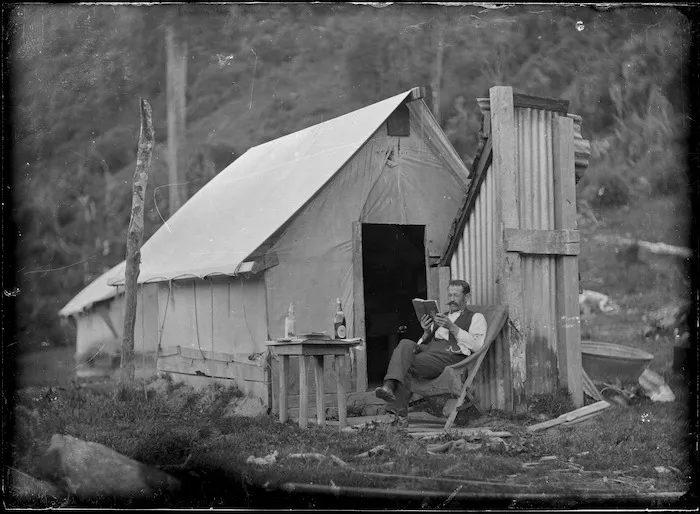 Man, sitting outside a hut, reading a book