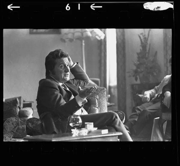 Patrick Macnee seated with brandy, coffee and cigarette