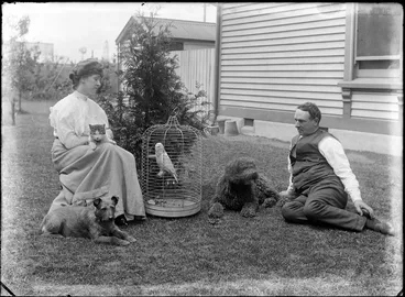 Image: Unidentified man and woman, with domestic pets outside a house, shows a cat, dogs and a parrot, probably Christchurch district