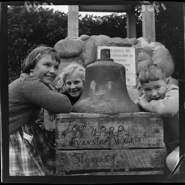 Image: Island Bay School pupils with a large bell that rests on a wooden crate, which has written on the side 'From Union Pacific Railroad, Evanston, Wyoming, United States'