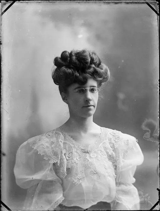 Unidentified woman wearing a lace top and glasses, with her hairstyle quite high, probably Hastings district