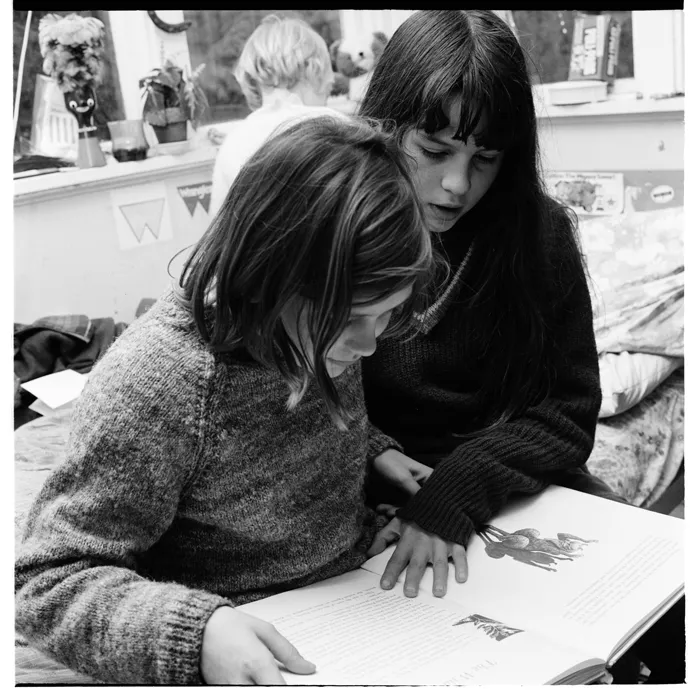 Two young girls reading a book together, and playing with toys