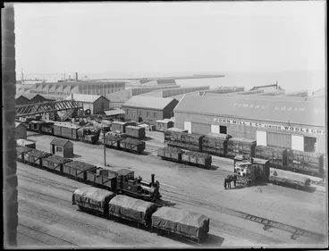 Image: John Mill and Company Ltd Wool and Grain Store, Timaru, with a steam train, freight carriages, horse and cart in the foreground