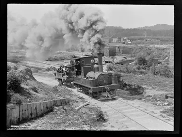 Image: William Williams with unidentified man on a steam train pulling a winching cable carriage, Kakahi Sawmill yard with logs and stacked cut timber beyond, Kakahi Settlement, Manawatu-Whanganui Region