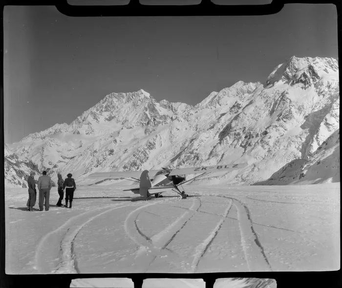 A Mount Cook Air Services Auster ZK-BLZ Ski Plane on the Tasman Glacier with unidentified people [Harry Wigley?], with Mount Cook beyond, Mount Cook National Park, Canterbury Region