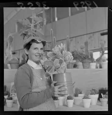 Image: Hutt Valley Horticultural Show, unidentified young girl holding a cactus with other cacti and succulents behind, Wellington Region