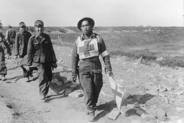 J A Gasson, fl 1945 (Photographer) : German prisoners bring in wounded under the cover of the Red Cross flag, carried by a member of the Maori Battalion, Senio River area, Italy