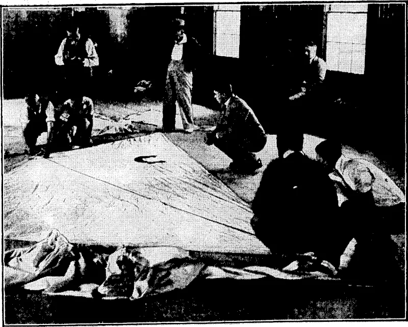 Evening Post" Photo. PREPARING FOR TODAY'S SANDERS CUP RAClNG.—Yesterday there was a busy scene at the Tamaki Yacht Club's pavilion, Auckland, where preparation ivas being made for the first race for the Sanders Memorial Cup, ivhich takes place today. The photograph shows officials measuring the sails of the competing boats. (Evening Post, 28 January 1936)
