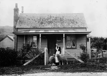 Image: Woman with two sheep outside a shingle roofed cottage