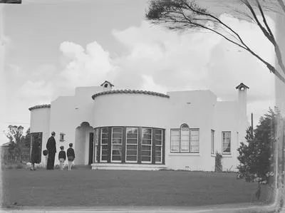 [Two young boys, a woman, and a man facing a house]