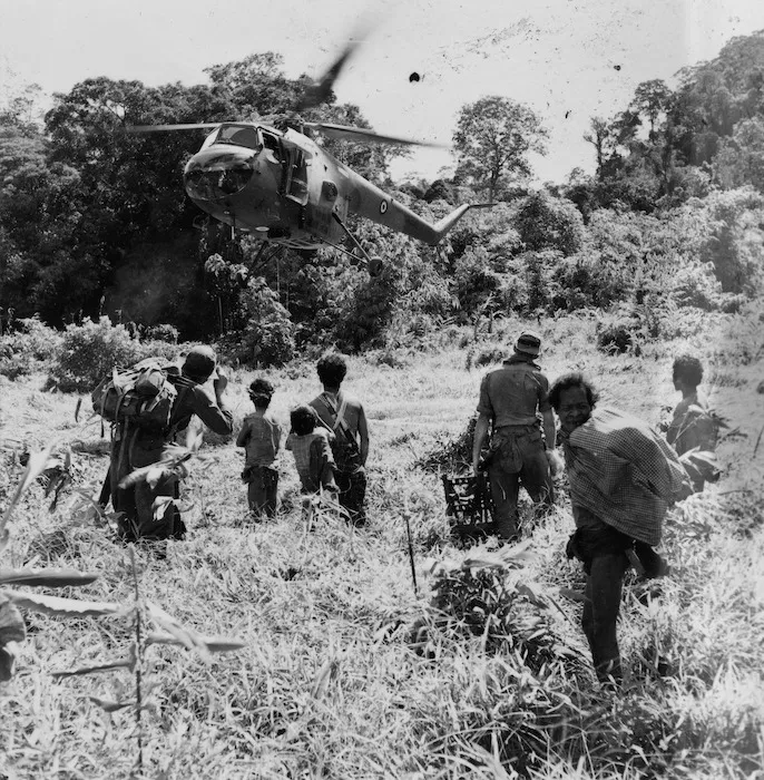 Local people and New Zealand troops watch a heliocopter land, Malaya