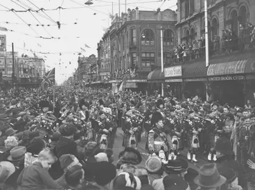 Image: Central City. Celebration. Victory in Europe or VE Day. Led by the Skirl of the Pipes Men March Through the "Bottleneck" and on to Cathedral Square. Crowds of Onlookers. Note This was celebrated on the 9 May, Two Days After the Actual Surrender As the Deputy Prime Minister, W. Nash, waited to Hear it Officially From Churchill. Colombo Street, Christchurch, Canterbury, New Zealand.