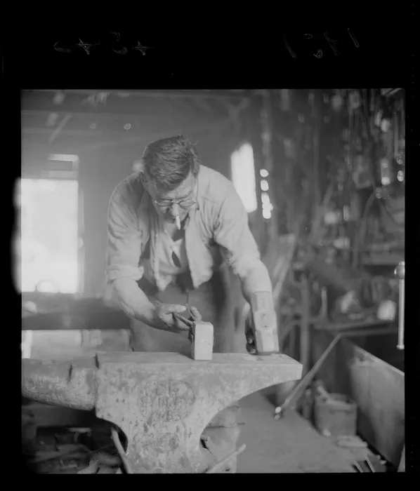 Unidentified blacksmith working at an anvil, in a workshop, Johnsonville, Wellington