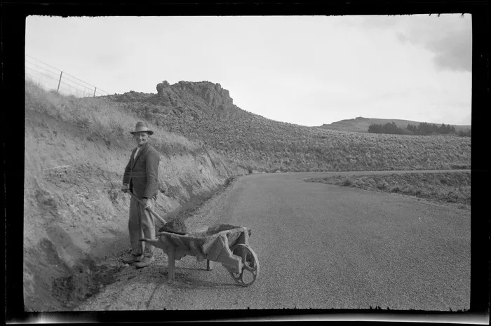 An unidentified man with a wheelbarrow digging a roadside drainage ditch near the top of the Port Hills Summit Road, Banks Peninsula, Canterbury Region
