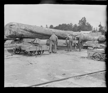 Image: Tree felling, three unidentified men using jacks to move a large log off a rail carriage, Kakahi Sawmill, Kakahi Settlement, Manawatu-Whanganui Region