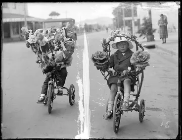 Image: Street scene, close-up view of two young boys on their tricycles decorated with flowers, Hawke's Bay District