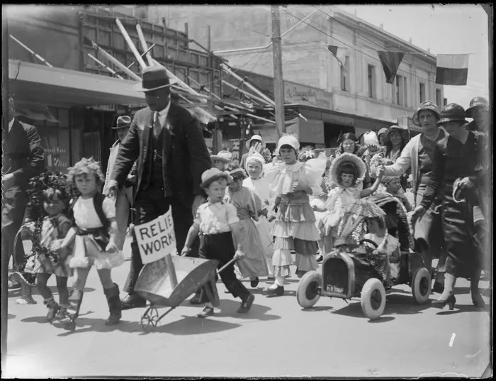 Unidentified children in fancy dress during the Napier parade been guided by adults, including one child pushing a relief workers wheelbarrow