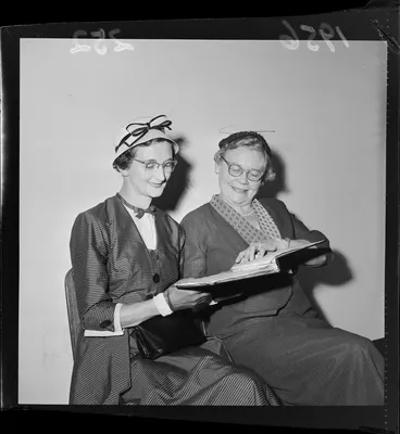 Image: Jean Allardyce and E M Matheson who are both dressed up in two-piece outfits that include a hat, a fascinator, gloves and glasses