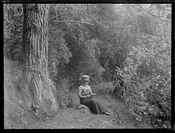 Lydia Williams, sitting on a rock, reading a book, surrounded by native bush, Te Aroha, Waikato District