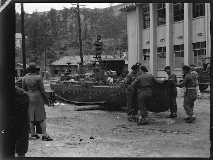 Men of 2NZEF Divisional Cavalry inspecting damaged model of Japanese battleship from naval academy on Eta Jima