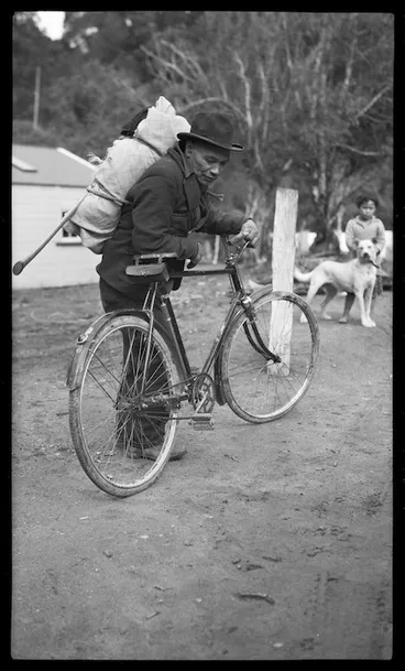 Image: Maori man with a swag on his back leaning against a bicycle