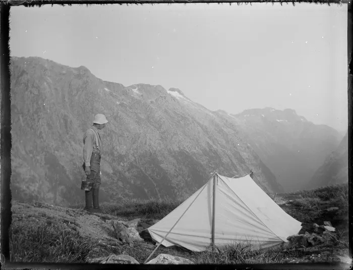 [Jack Murrell] standing outside a tent during Edgar Williams and Jack Murrell's climbing expedition, Fiordland National Park, South Island