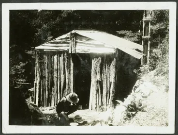 Image: Tawhai Hut. [Image of a man crouching outside a wooden hut.]