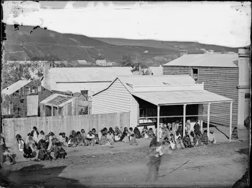 Image: Group of people sitting in a line outside a shop in the Wanganui area, possibly waiting for a land court hearing