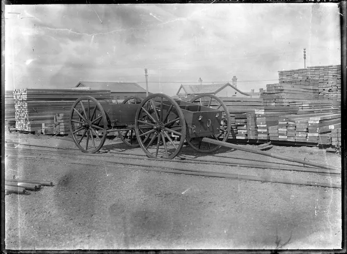 A timber yard with piles of sawn timber, and a cart in the foreground.