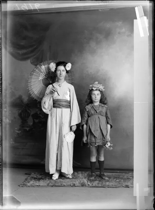 Studio portrait of two unidentified girls in costume, one girl in Japanese kimono and holding a parasel, probably Christchurch district