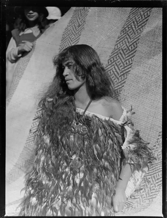 Annie Ngauru Hoko (nee Downs) standing by a whariki flax mat with woven design, Tokaanu