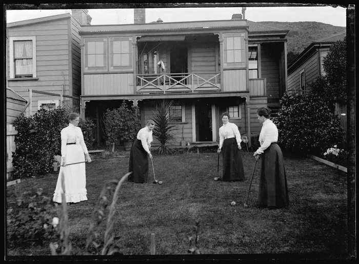 Four women playing croquet in the backyard of a house