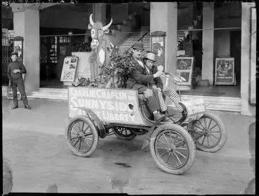 Image: Mr Leonard Doogood, Charlie Chaplin impersonator, in an Oldsmobile motor car, outside the Liberty Theatre, Cathedral Square, Christchurch