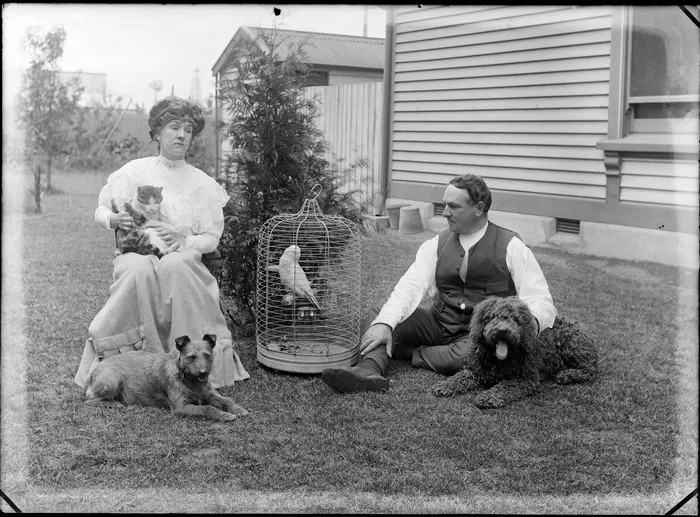 Unidentified man and woman, with domestic pets outside a house, shows a cat, dogs and a parrot, probably Christchurch district