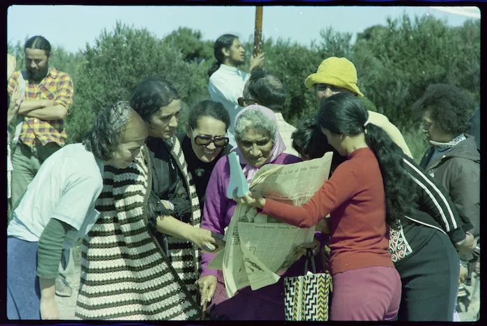 Titewhai Harawira, Carmen Kirkwood, Whina Cooper, and Hana Jackson reading a newspaper on the road