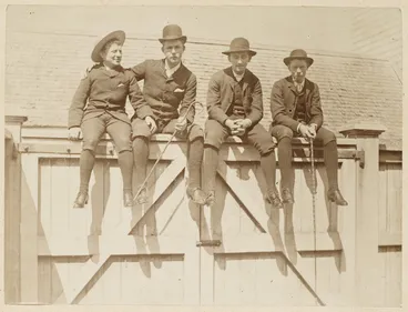 Image: Four men sitting on top of a gate